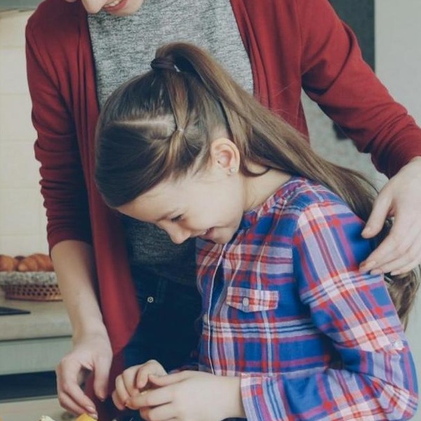 A young girl focused on drawing at the kitchen table, pencils and a cup of herbs beside her